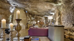 Ein Zimmer mit Steinwand, einem violetten Sofa, einem Holztisch mit Büchern und einer Bar mit einer Lampe.