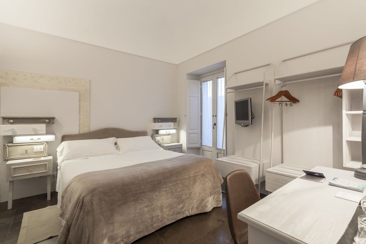 Ein Hotelzimmer mit einem Bett, Nachttischen, einem Schreibtisch, einem Sessel, einem Fernseher und einem Kleiderschrank.