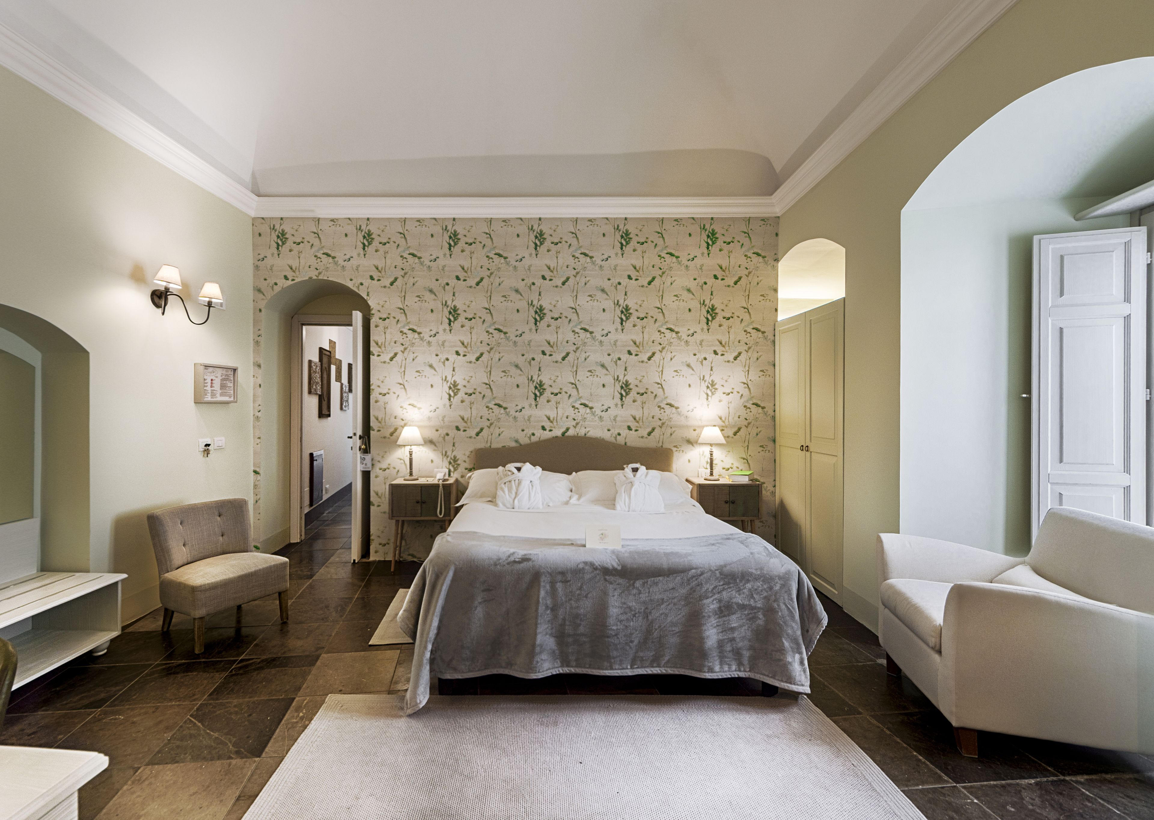 A hotel room with a large bed, two bedside tables with lamps, a chair, a desk, and a mirror.