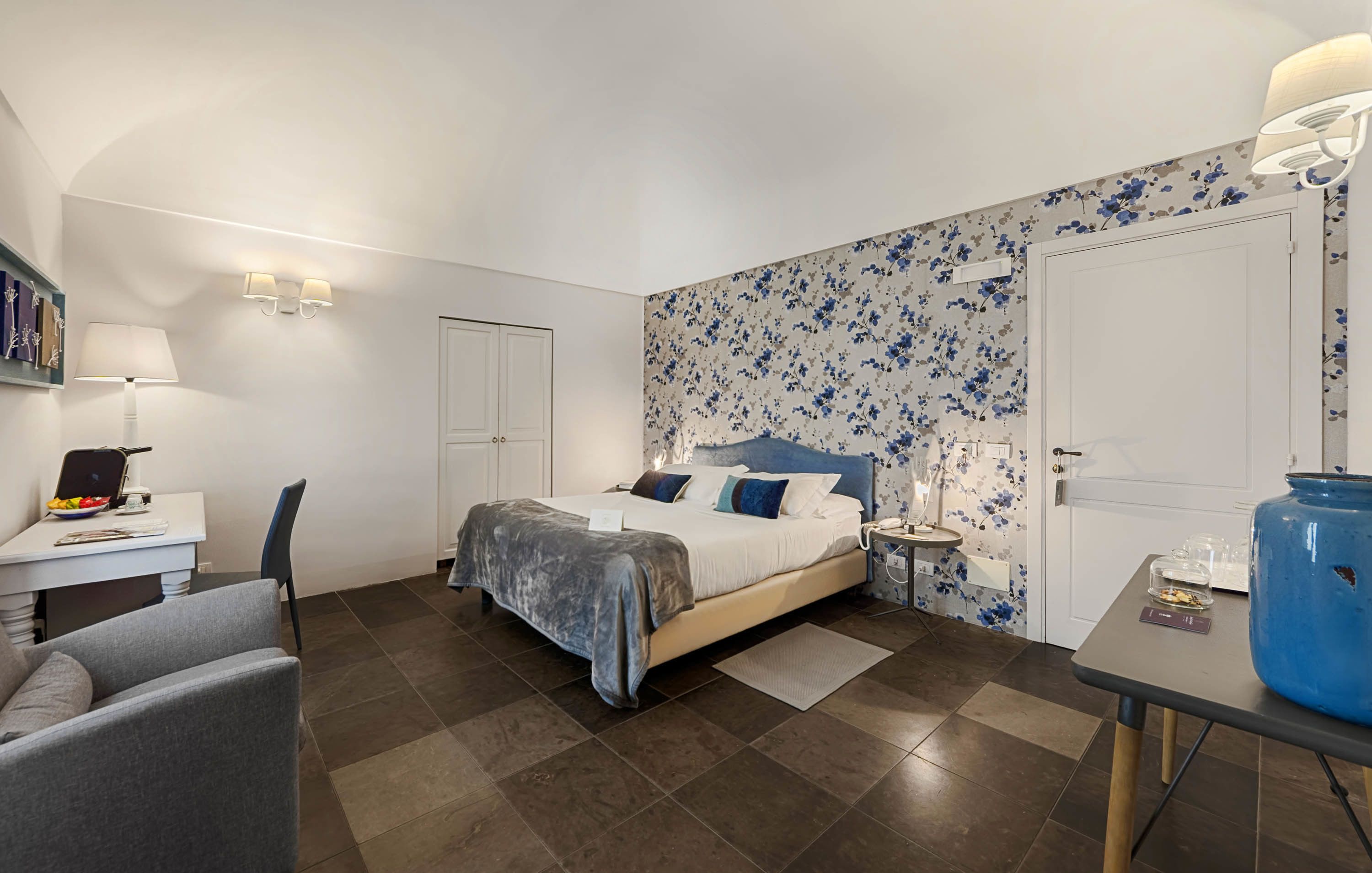 A bedroom with a bed, bedside table, lamp, chair, and a desk with a lamp.