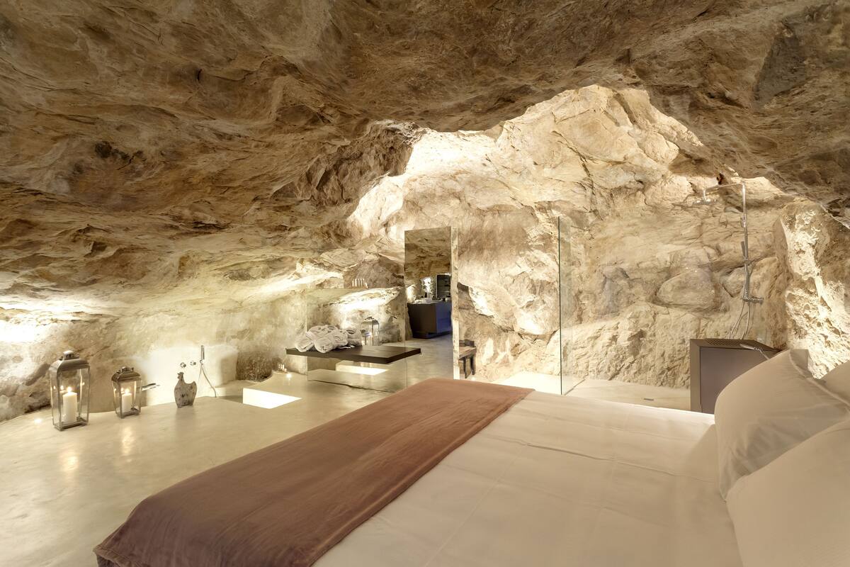 Ein Schlafzimmer mit einer gewölbten Decke, die an eine Steinhöhle erinnert, einem Bett, Nachttischen und einer kleinen Sitzecke.