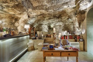 Una zona de bar con techo de piedra rústica, mobiliario de madera y diversos utensilios y botellas.
