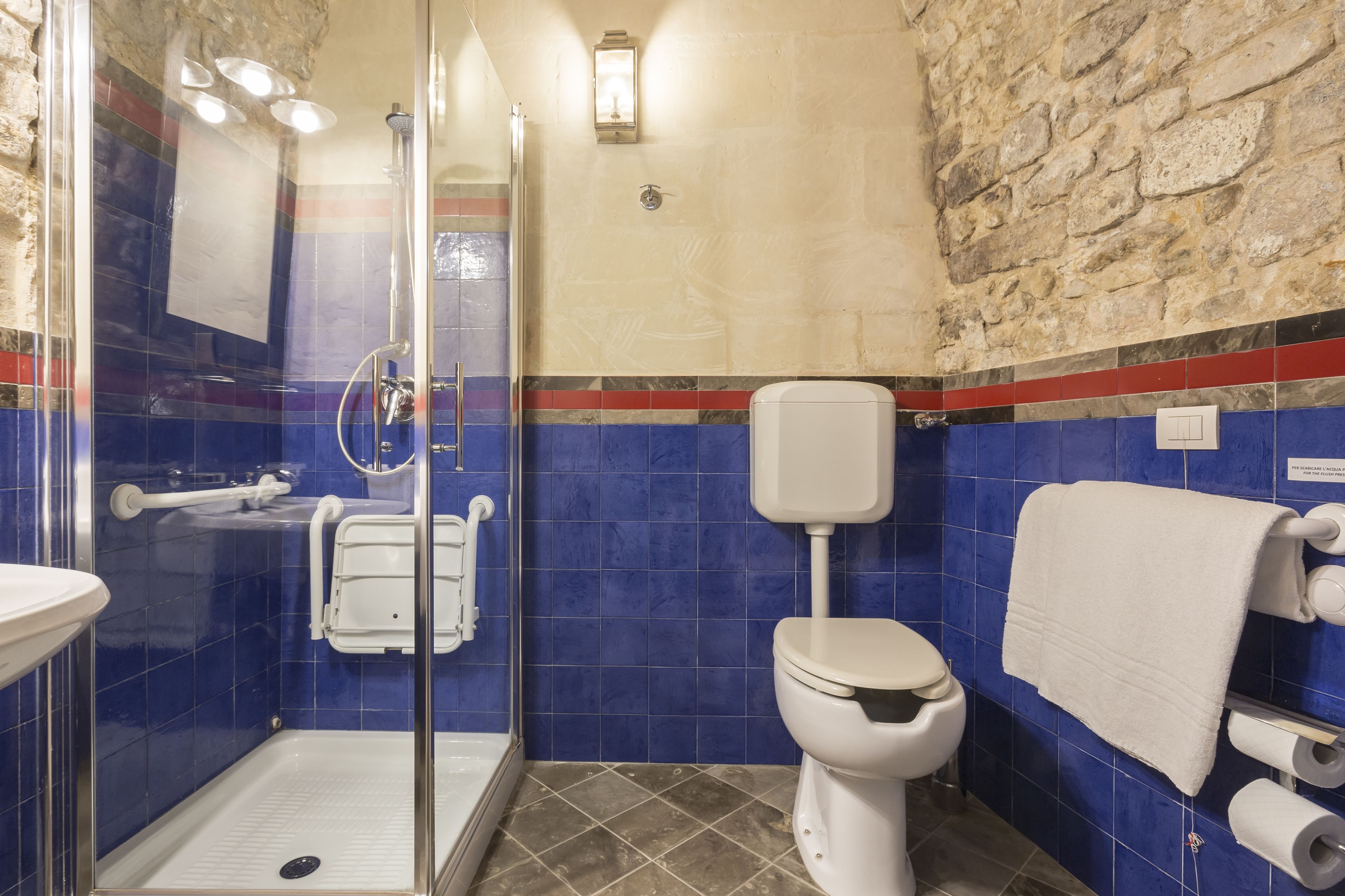 Un baño con cabina de ducha de vidrio, inodoro blanco, paredes con azulejos azules y una pared de acento de piedra.