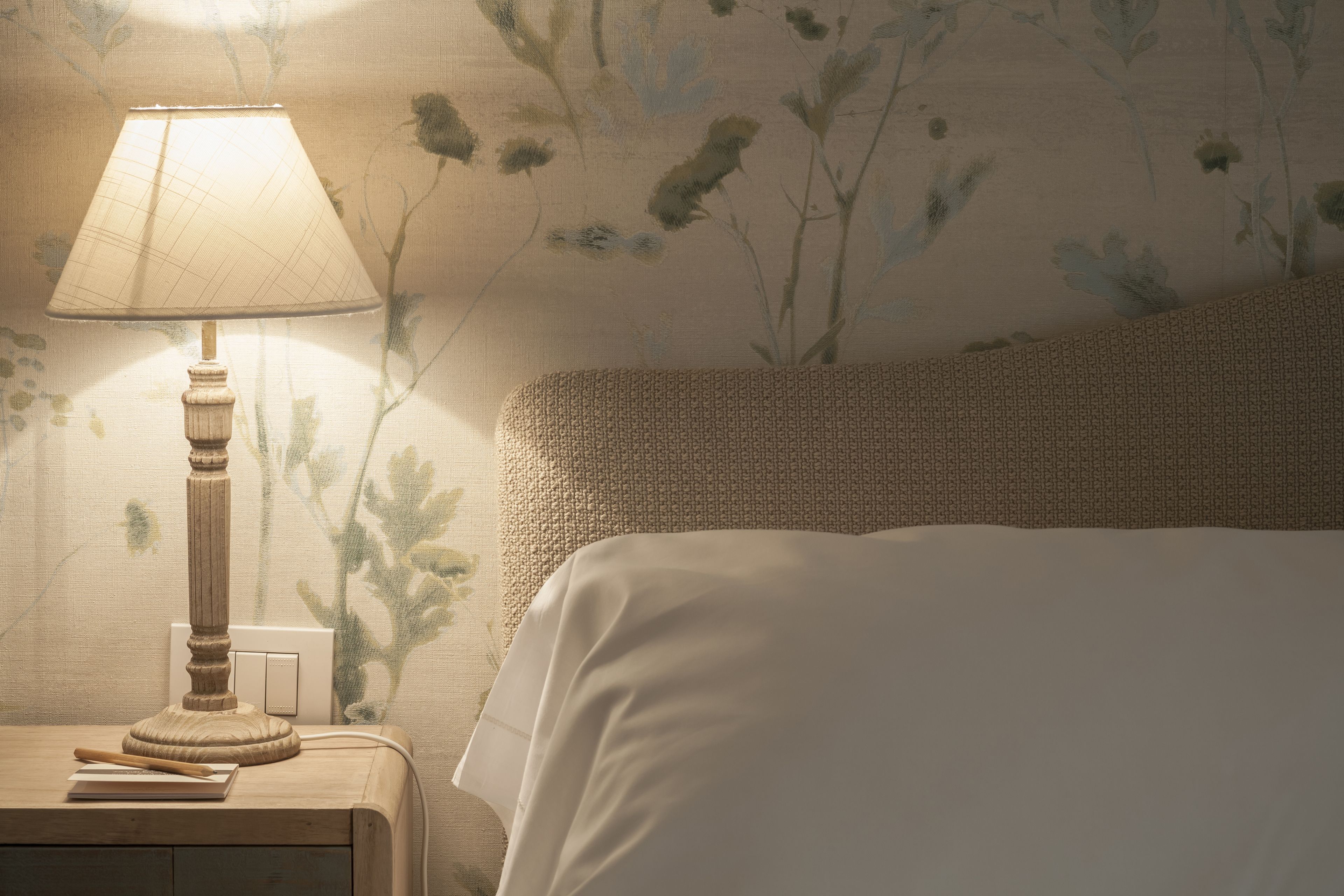 A bedroom with a bedside table, lamp, and a bed with a textured headboard.