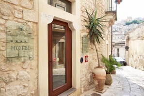 Un edificio de piedra con puerta de madera, un cartel que indica que es un hotel y plantas en macetas en el suelo.