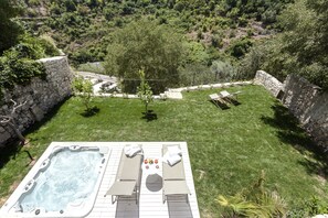Un jacuzzi con dos sillones reclinables y una mesa, rodeado de un césped cuidado y muros de piedra.