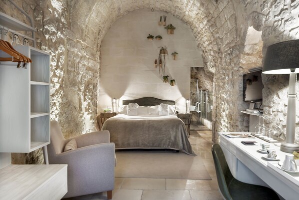 Un dormitorio con pared de piedra, cama, silla, escritorio y lámpara.