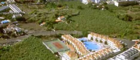 Vista aérea de un resort con piscina, cancha de tenis y propiedades frente a la playa.
