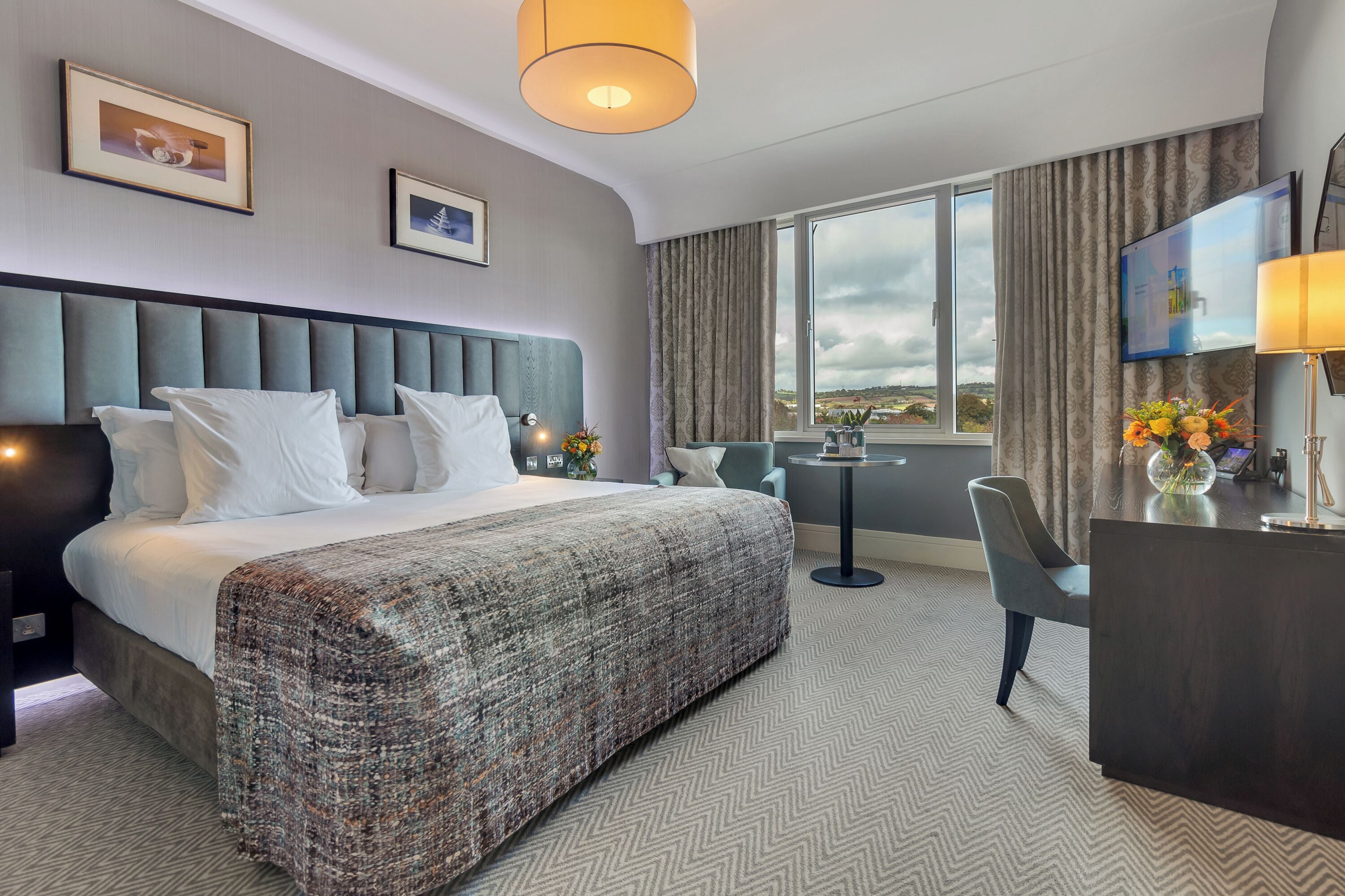 A hotel room with a large bed, a desk, a chair, and a view of the outdoors.