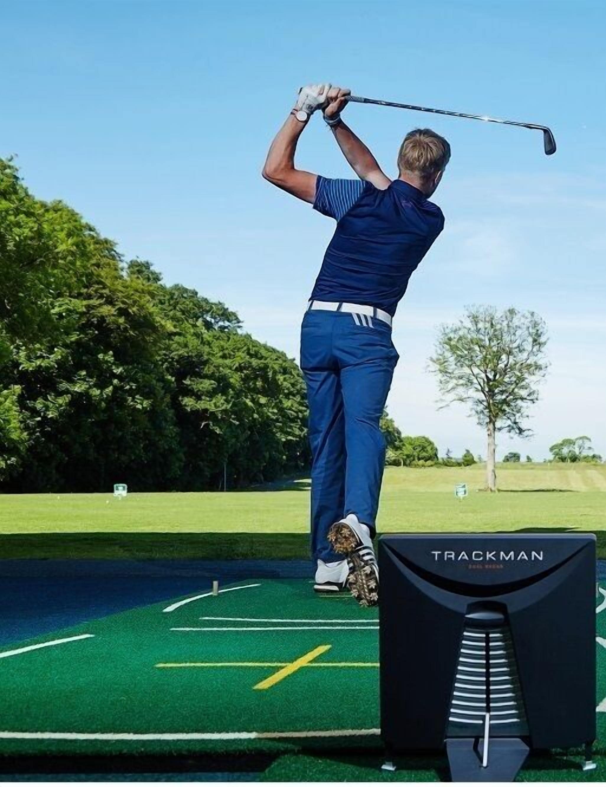 Una persona juega al golf en un campo verde con árboles al fondo.