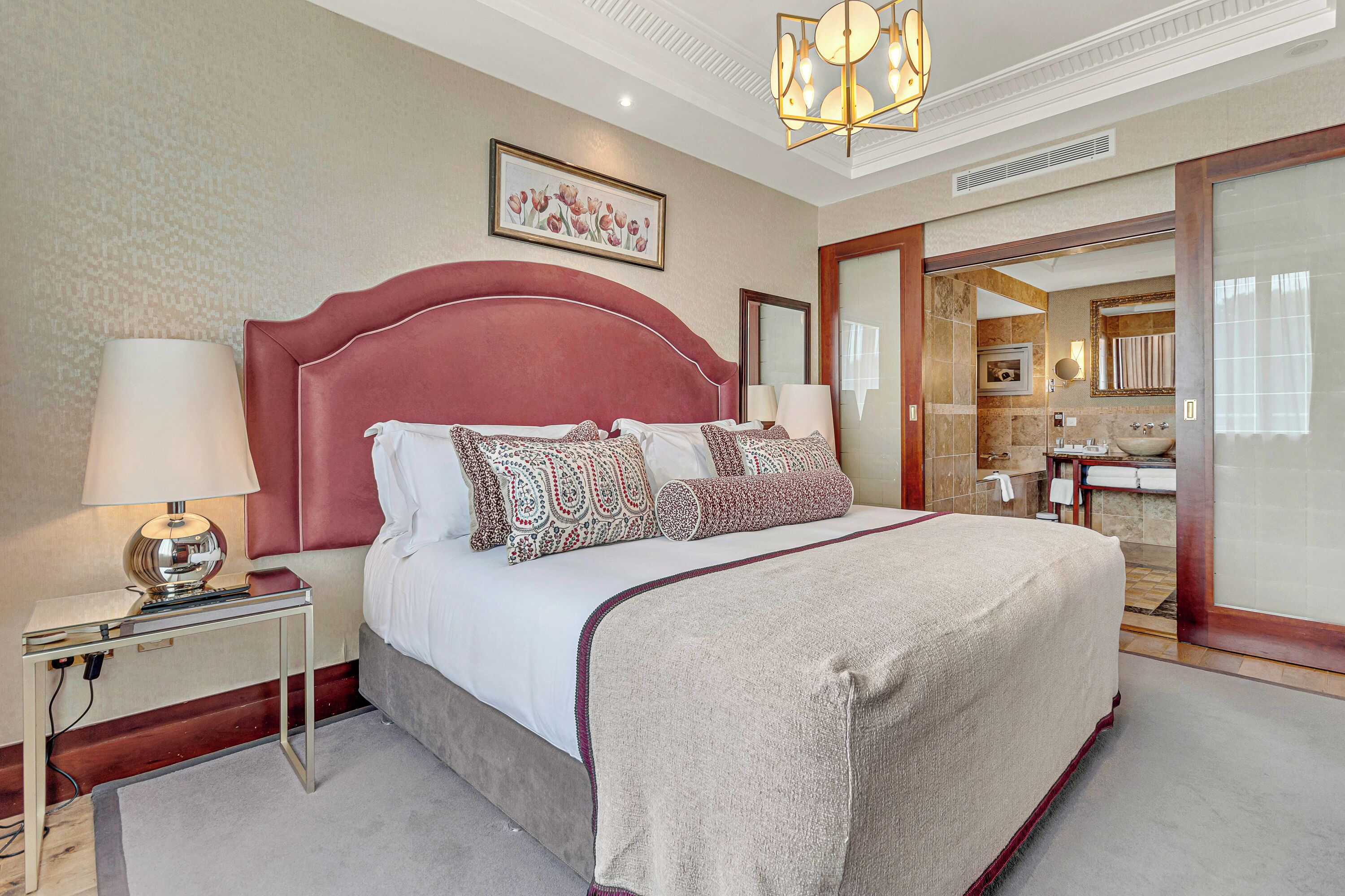 A spacious bedroom with a large bed, a bedside table with a lamp, and a mirror.