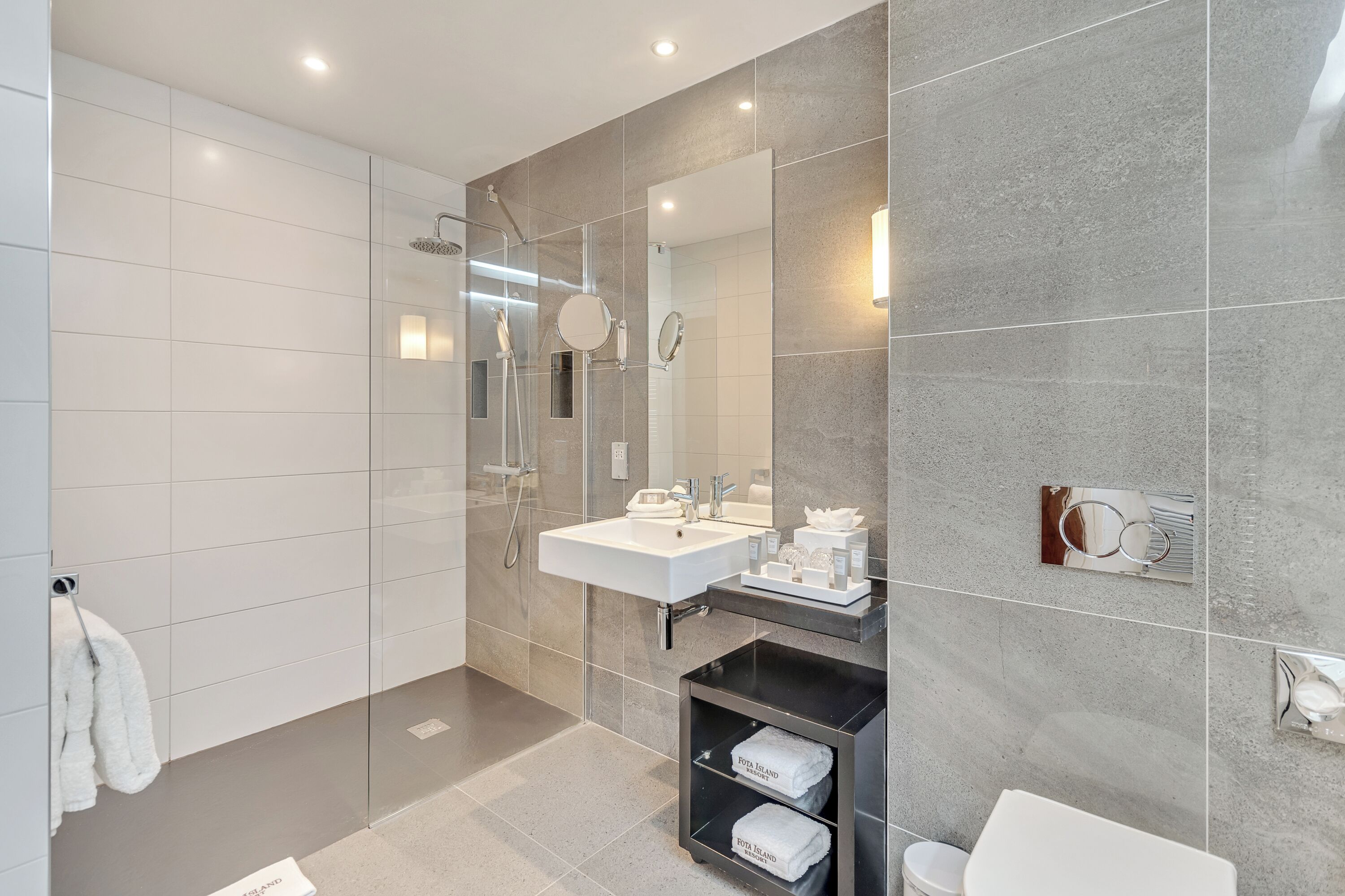 Un baño moderno con ducha de vidrio, lavamanos blanco y un espejo grande.