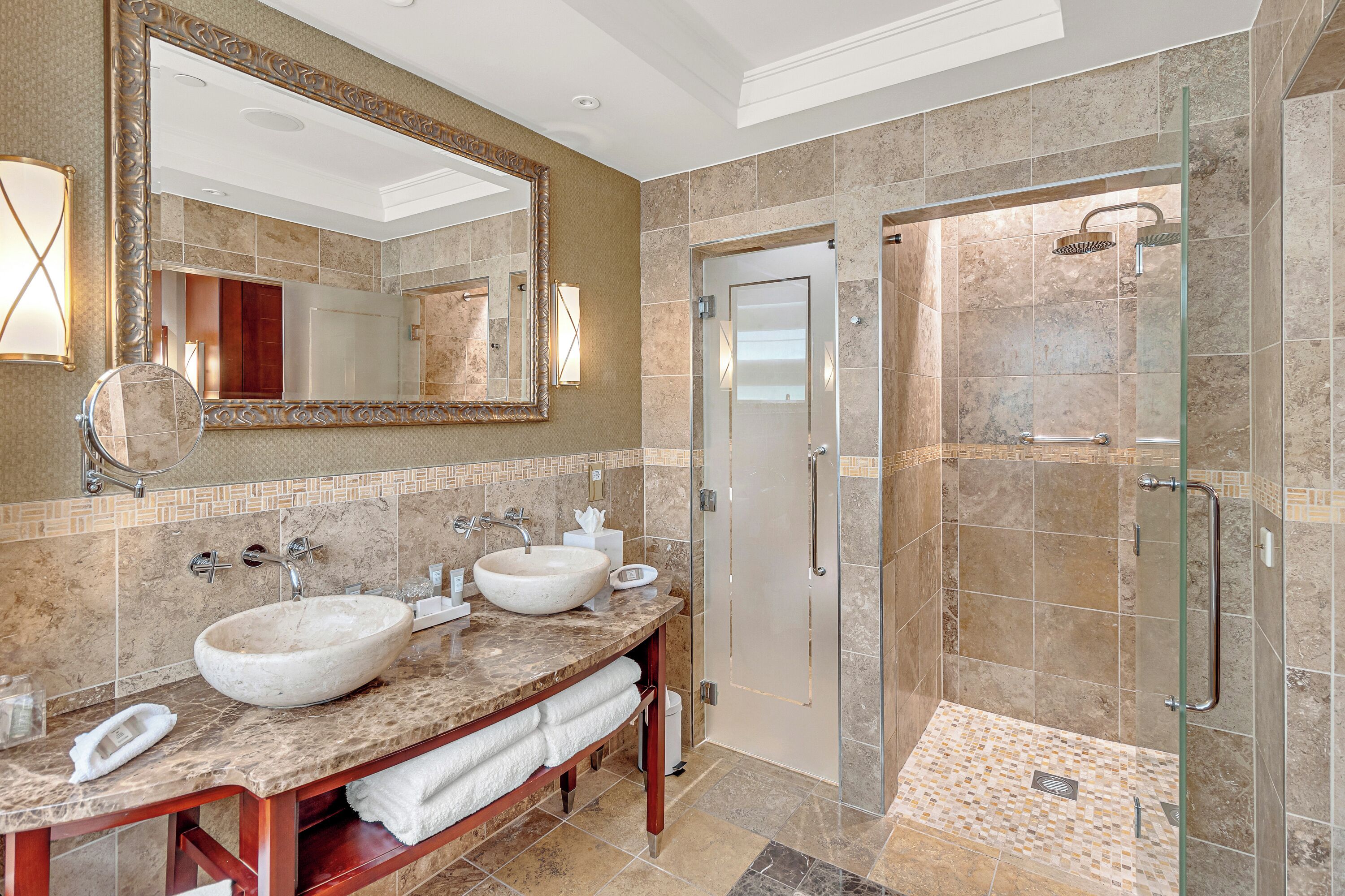 A bathroom with a large mirror, two sinks, a glass shower enclosure, and a tiled floor.