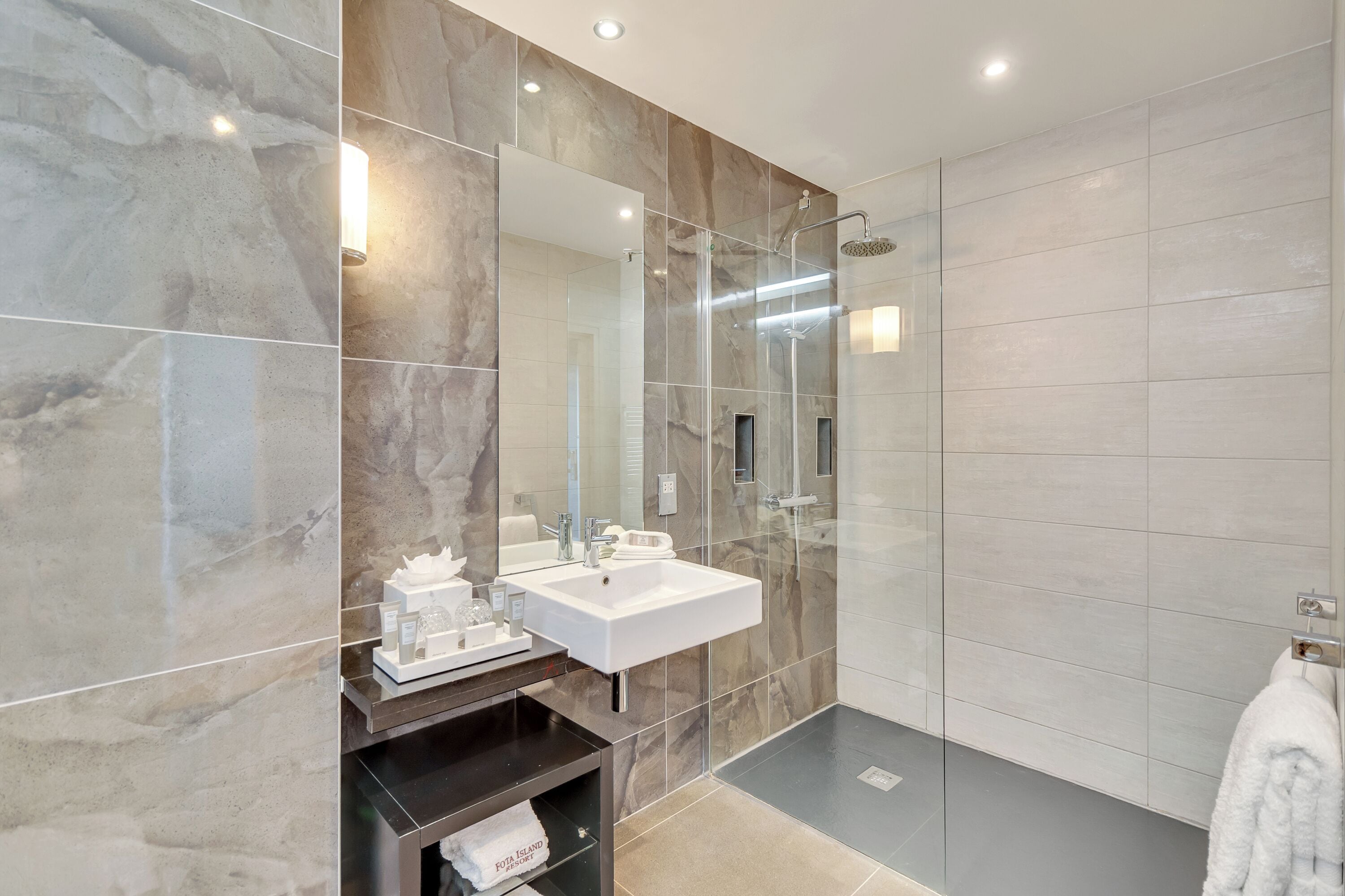 Un baño moderno con pared de mármol, lavamanos blanco, cabina de ducha de vidrio y barra para toallas.
