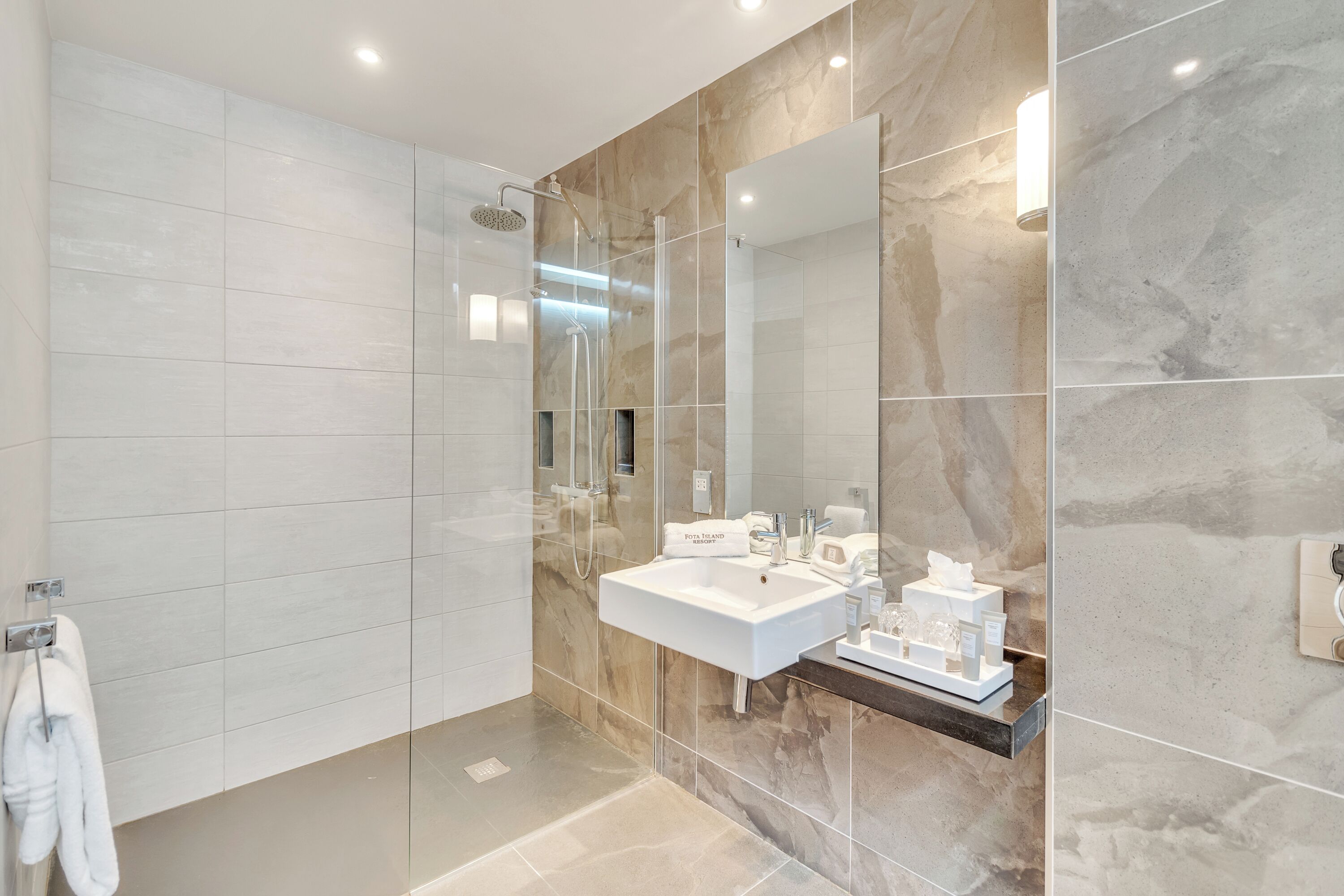 Un baño moderno con un espejo grande, un lavamanos y una ducha.