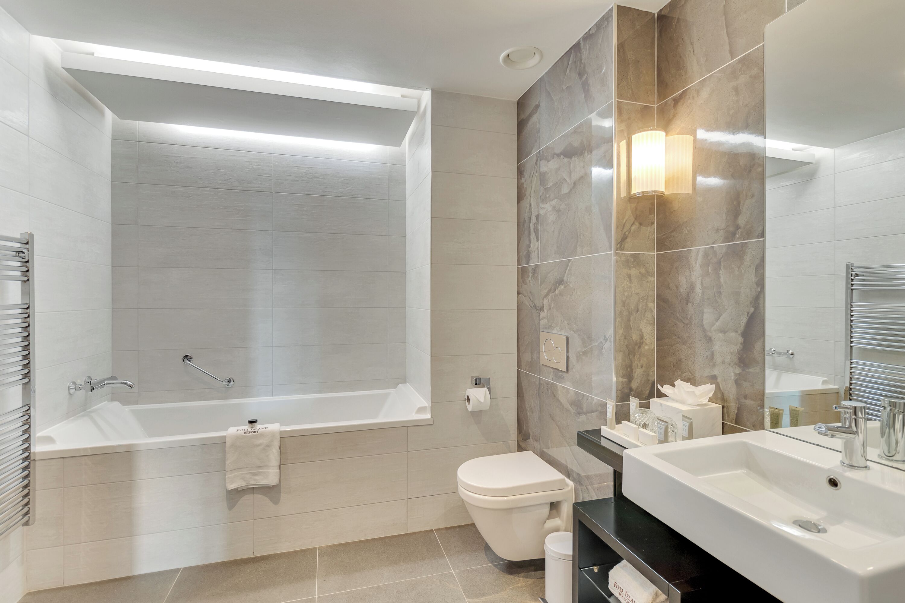 Un baño moderno con bañera, inodoro y un espejo grande.
