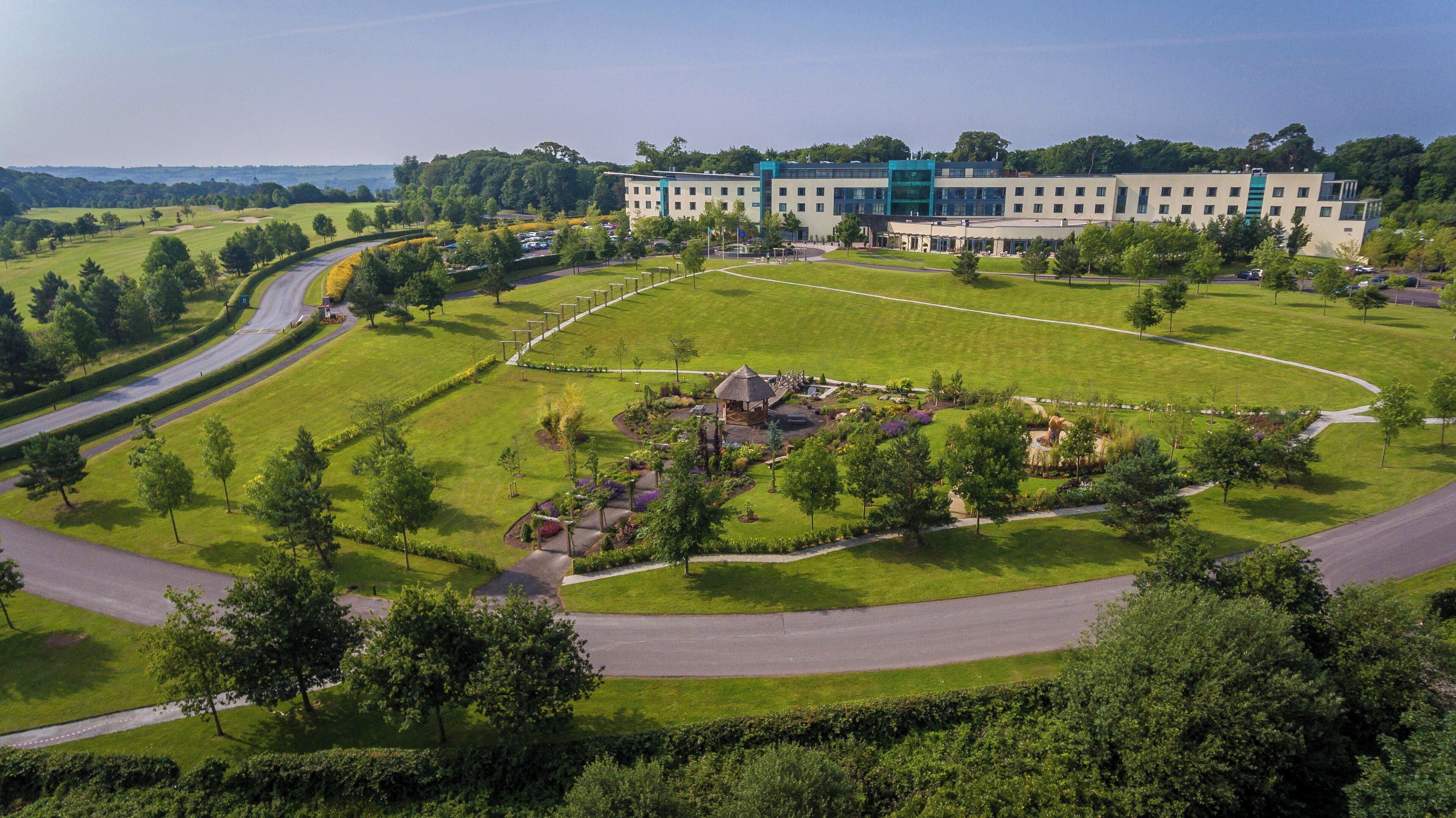 A modern building with a large lawn, a pavilion, and a curved road.