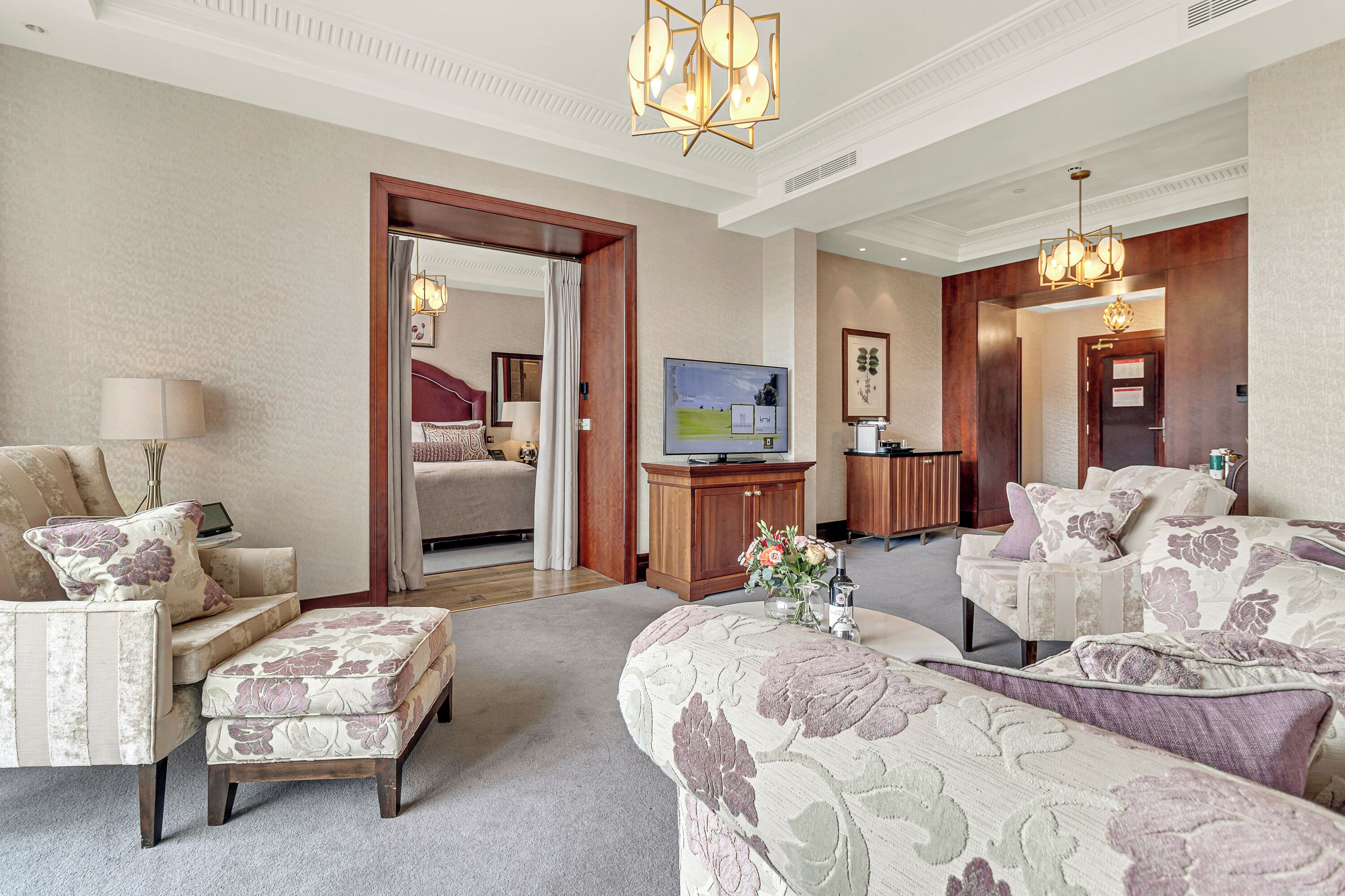 A spacious hotel room with a large bed, two armchairs, a sofa, a television, and a wooden cabinet.