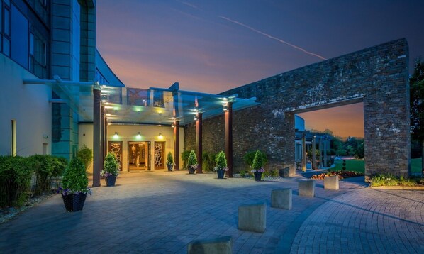 A hotel entrance with a modern glass facade, a stone archway, and a paved courtyard. - Fota Island Hotel & Spa (Fota)