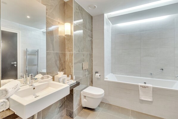 Un baño moderno con una bañera grande, un inodoro separado y un tocador con lavamanos y espejo.