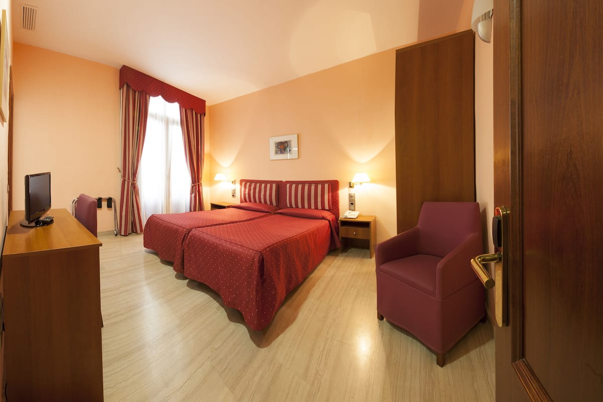 A hotel room with a bed, a desk with a computer, a chair, and a door.