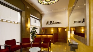 Un hall de hotel con asientos rojos, un mostrador de recepción y una lámpara de araña grande.