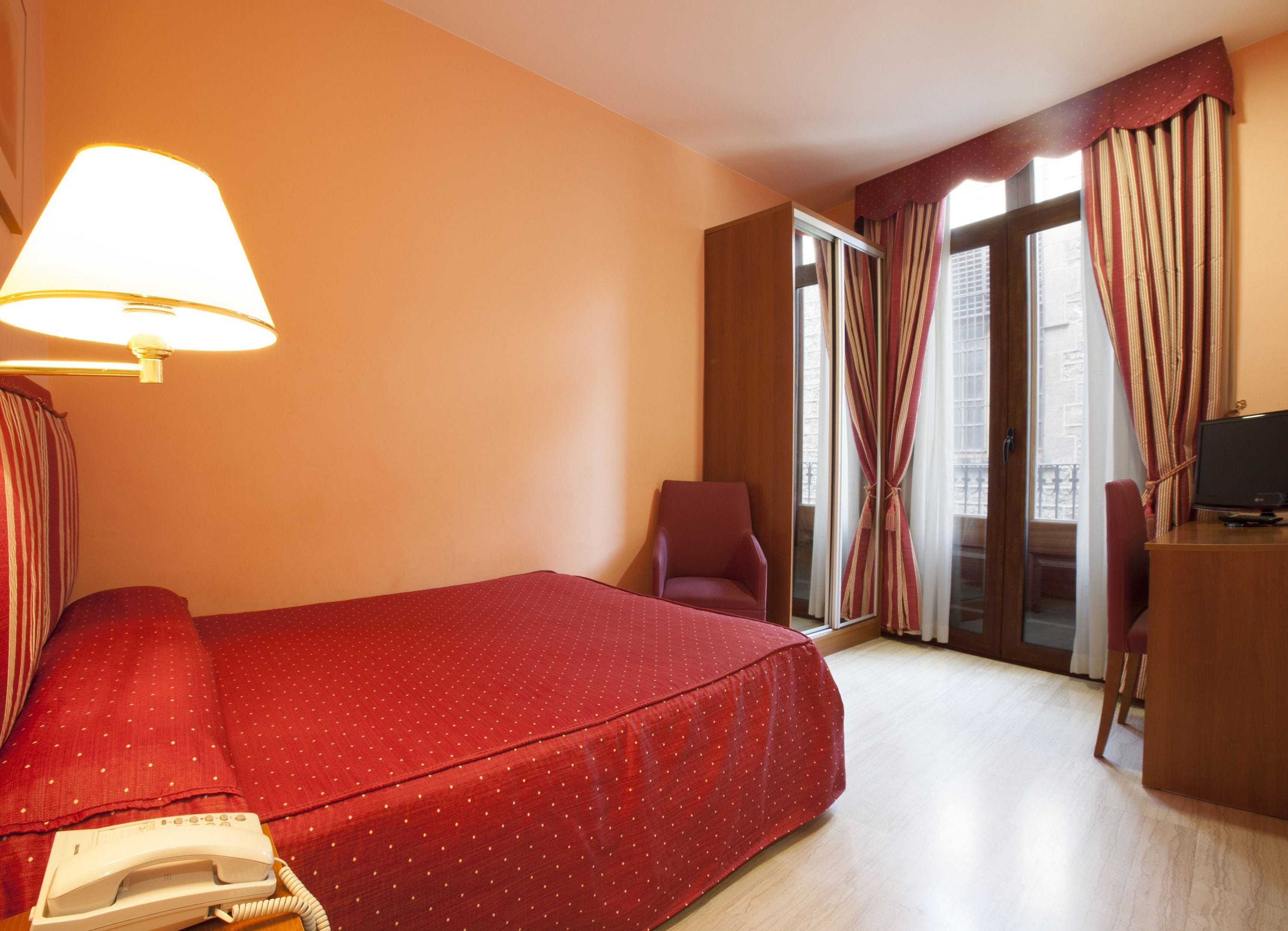 A hotel room with a bed, a desk, a chair, a lamp, and a telephone.