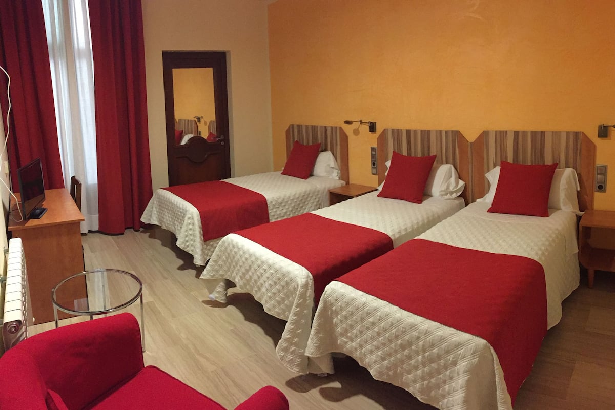 A hotel room with two beds, each with a red and white bedspread, a small table, a chair, and a mirror on the wall.