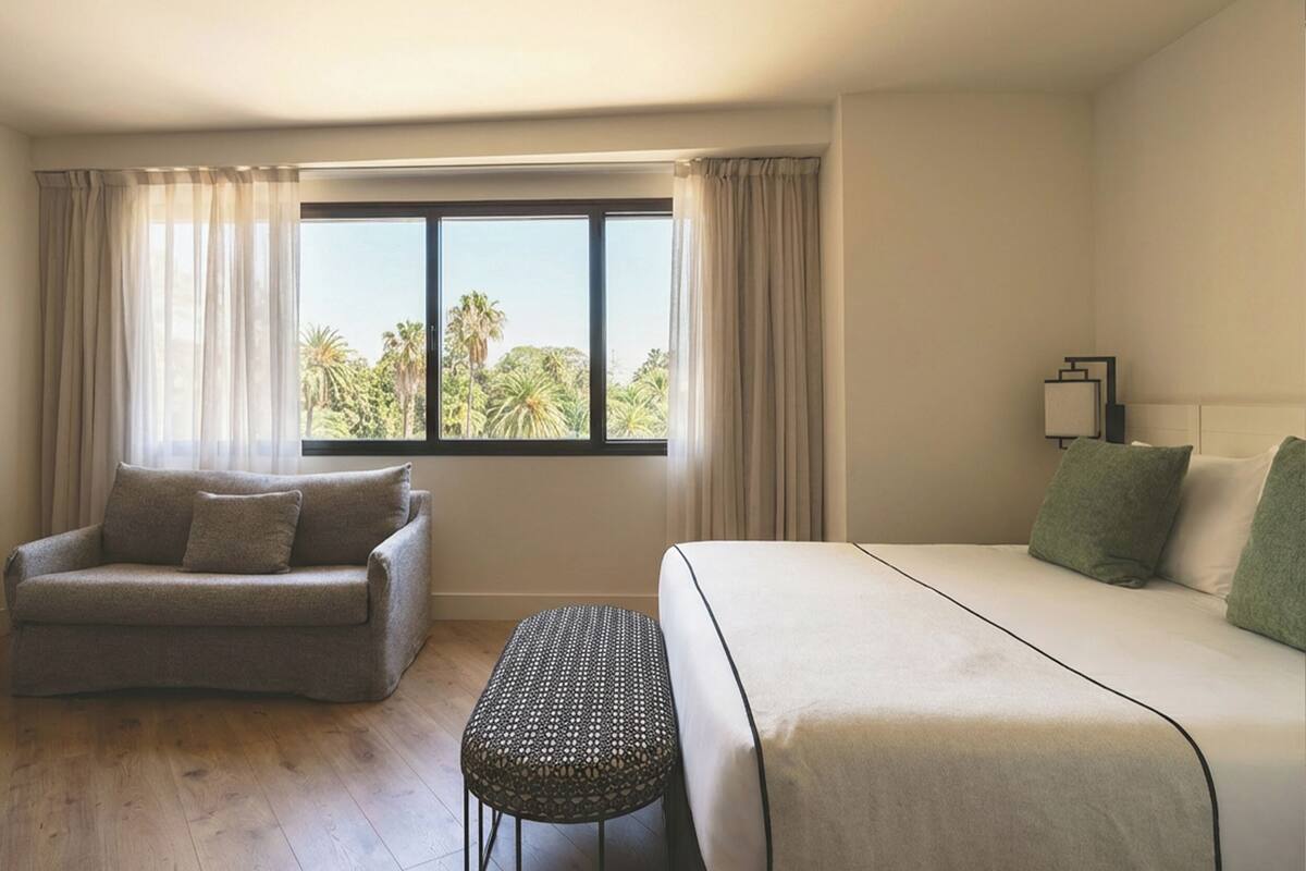 Una habitación de hotel con cama, sofá, una mesita y ventana con cortinas.