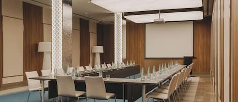 Une salle de conférence avec une longue table, des chaises, un écran de projection et un sol recouvert de moquette.