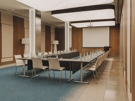 A conference room with a long table, chairs, a projector screen, and a carpeted floor.