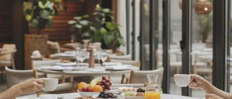A breakfast setting with a table set for two, featuring bread, fruits, and a glass of orange juice.