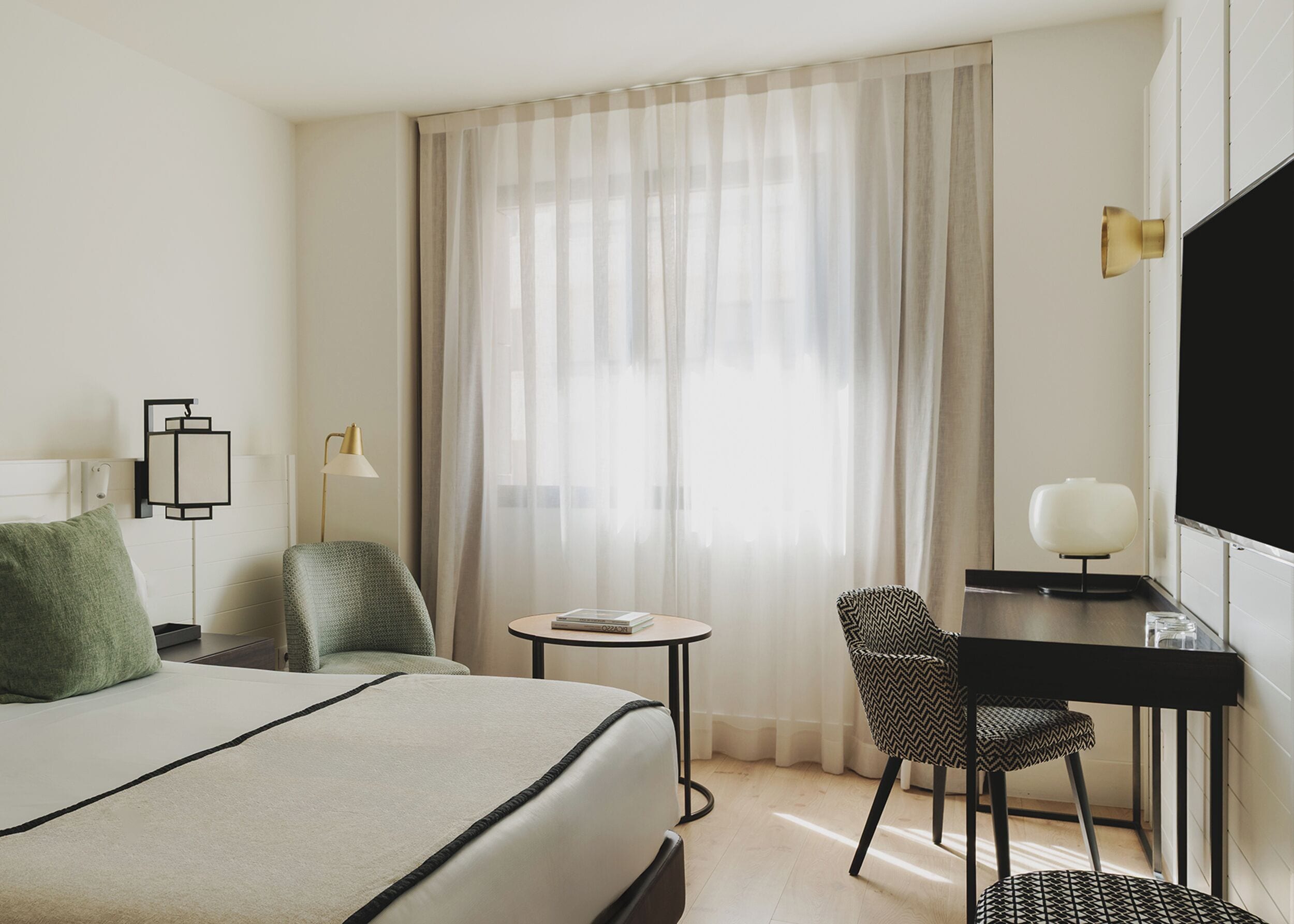 Une chambre d’hôtel avec un lit, un bureau, une chaise, une télévision et une fenêtre avec des rideaux.