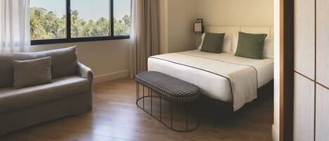 A hotel room with a bed, a sofa, a bench, and a window with curtains.