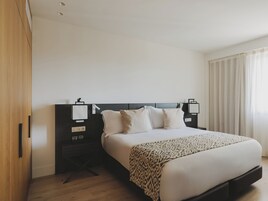 Une chambre d’hôtel moderne avec un grand lit, une armoire en bois, une table de chevet avec une lampe et une fenêtre avec des rideaux.