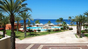 Une piscine d’un complexe hôtelier offrant une vue dégagée sur l’océan, entourée de palmiers et de chaises longues.