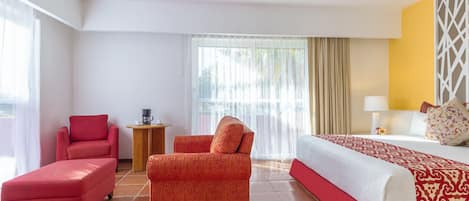 A hotel room with a bed, two red chairs, a small table with a coffee maker, and a window with curtains.