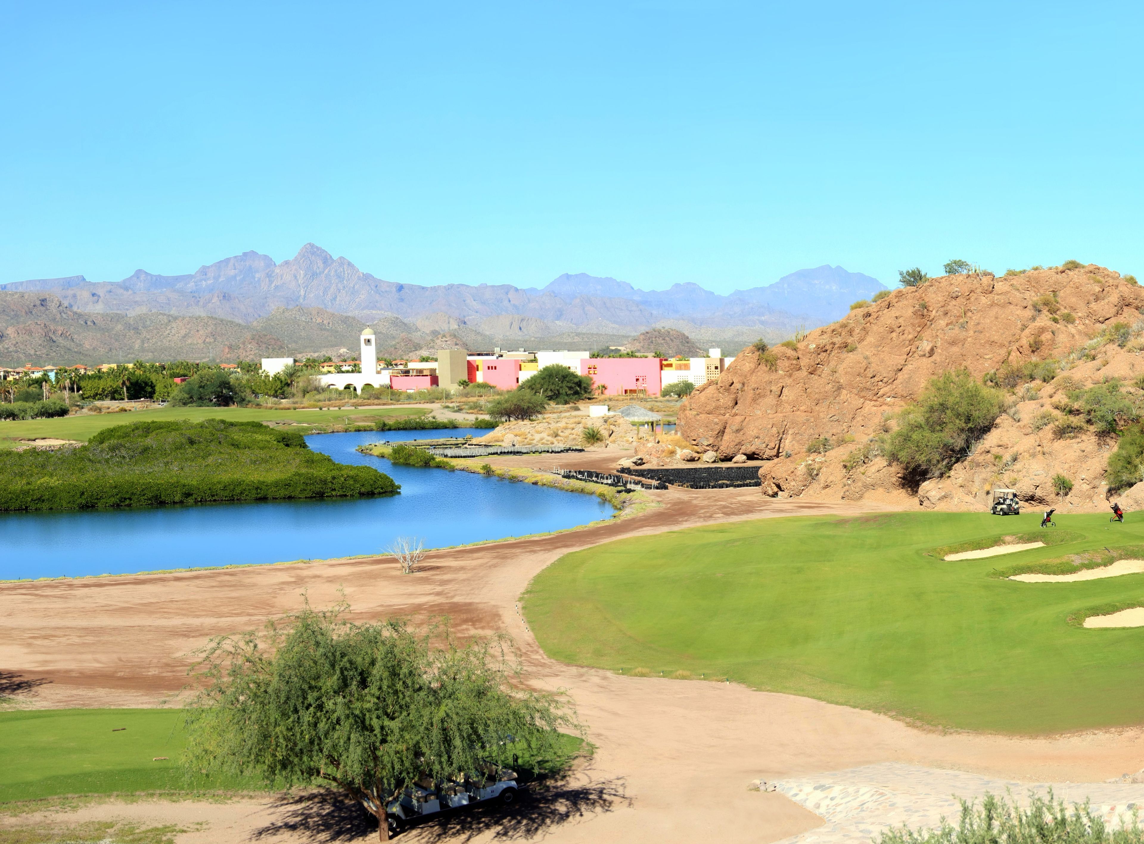 A golf course with a water body, green areas, and a mountainous backdrop.