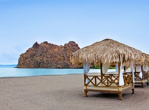 Una playa con cabañas de techo de paja y un acantilado rocoso al fondo.