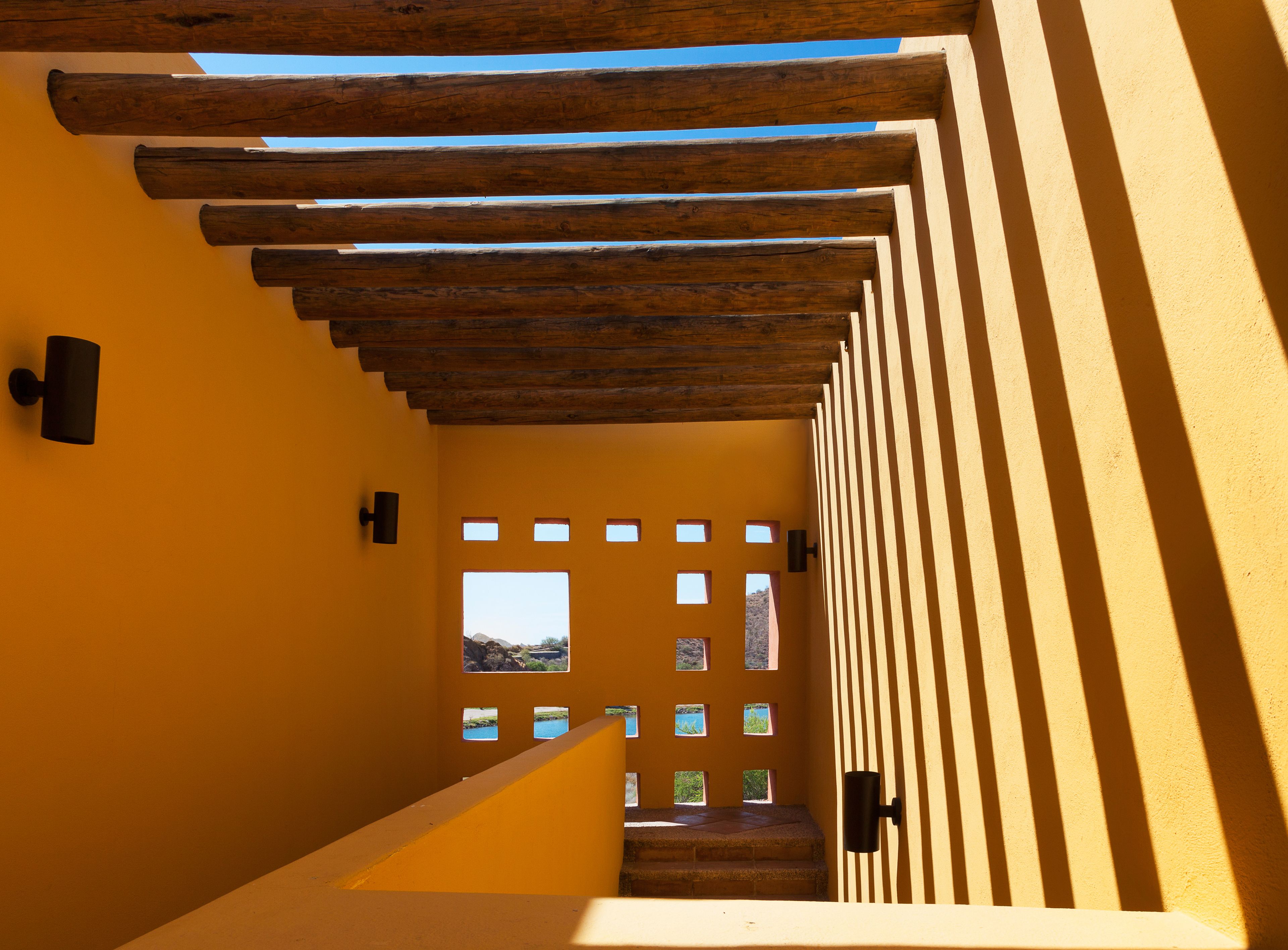 Ein Korridor mit Holzbalken und gelber Wand, der zu einer Tür mit mehreren Fenstern führt.