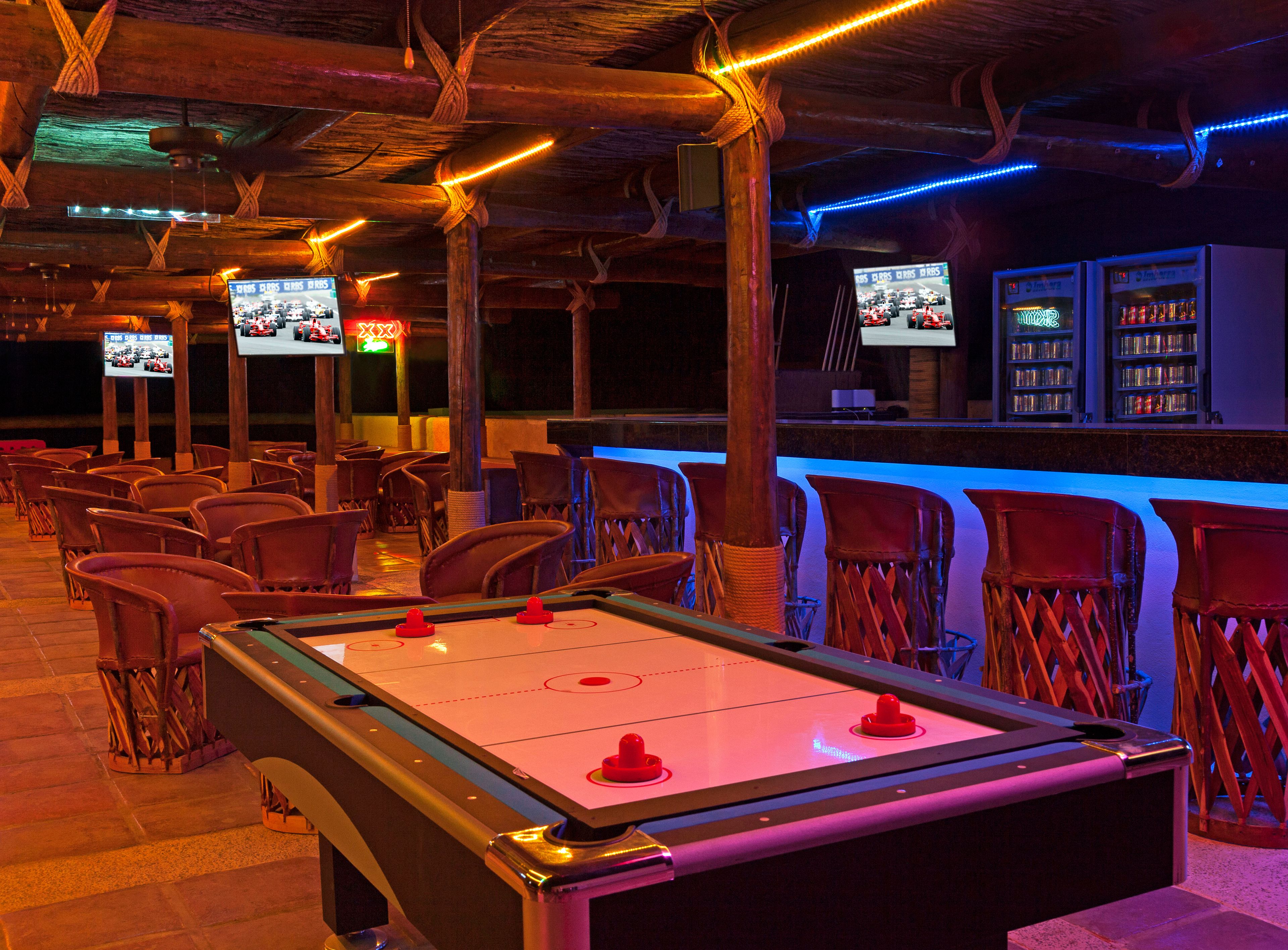 A bar area with a foosball table, multiple TV screens, and bar stools.