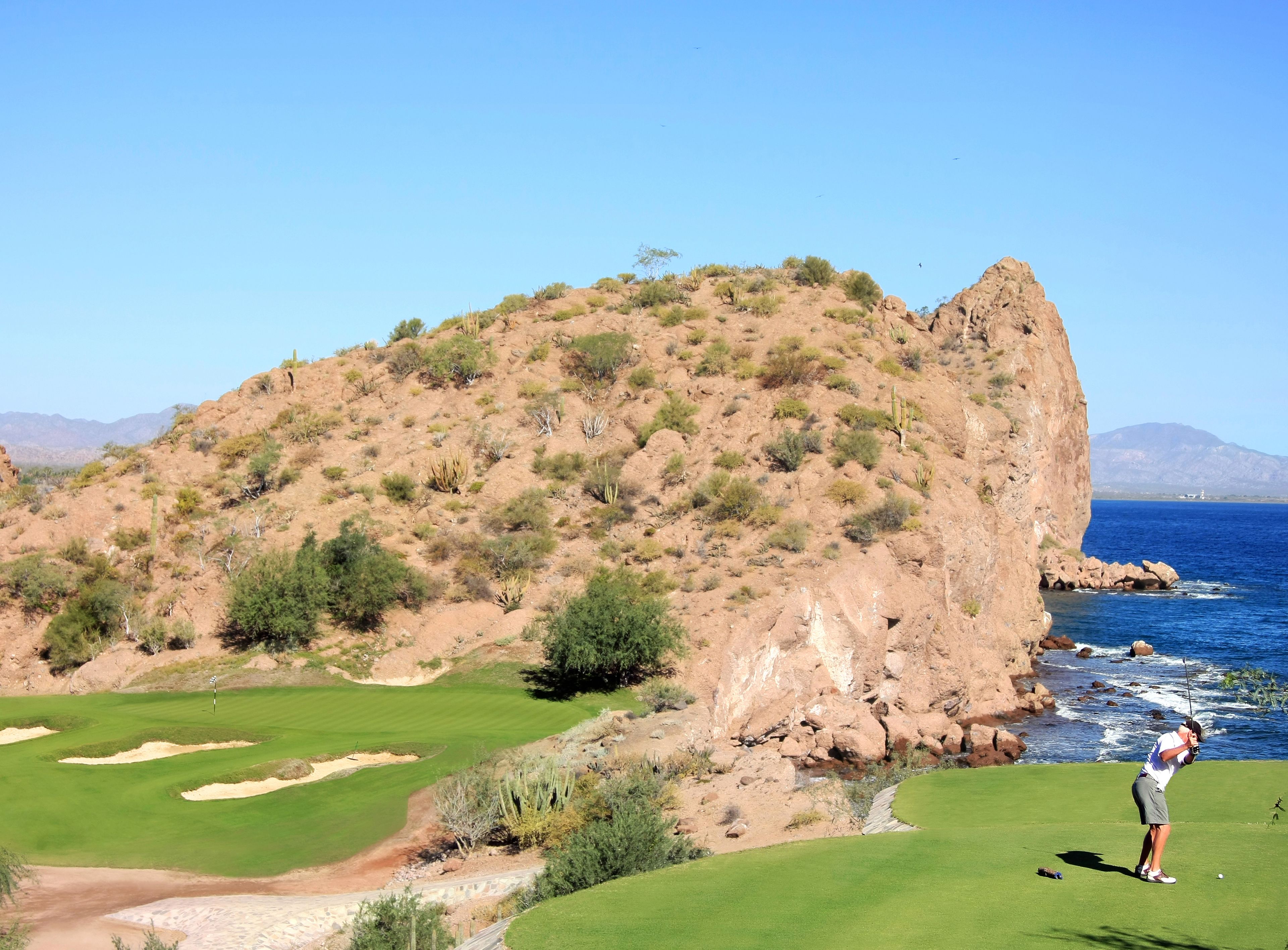 Un campo de golf con vistas al océano y montañas al fondo.