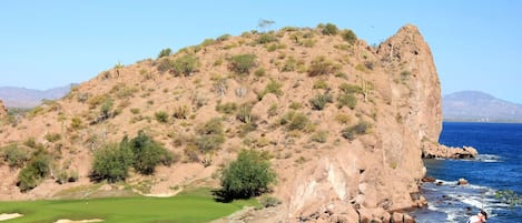 Un campo de golf con vistas al océano y montañas al fondo.