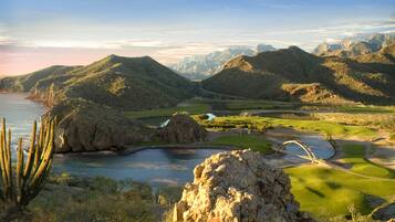 Un paysage montagneux comprenant un terrain de golf, une étendue d’eau et une grande formation rocheuse.