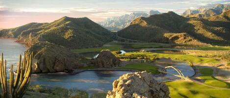 Paisaje montañoso con un campo de golf, una masa de agua y una gran formación rocosa.