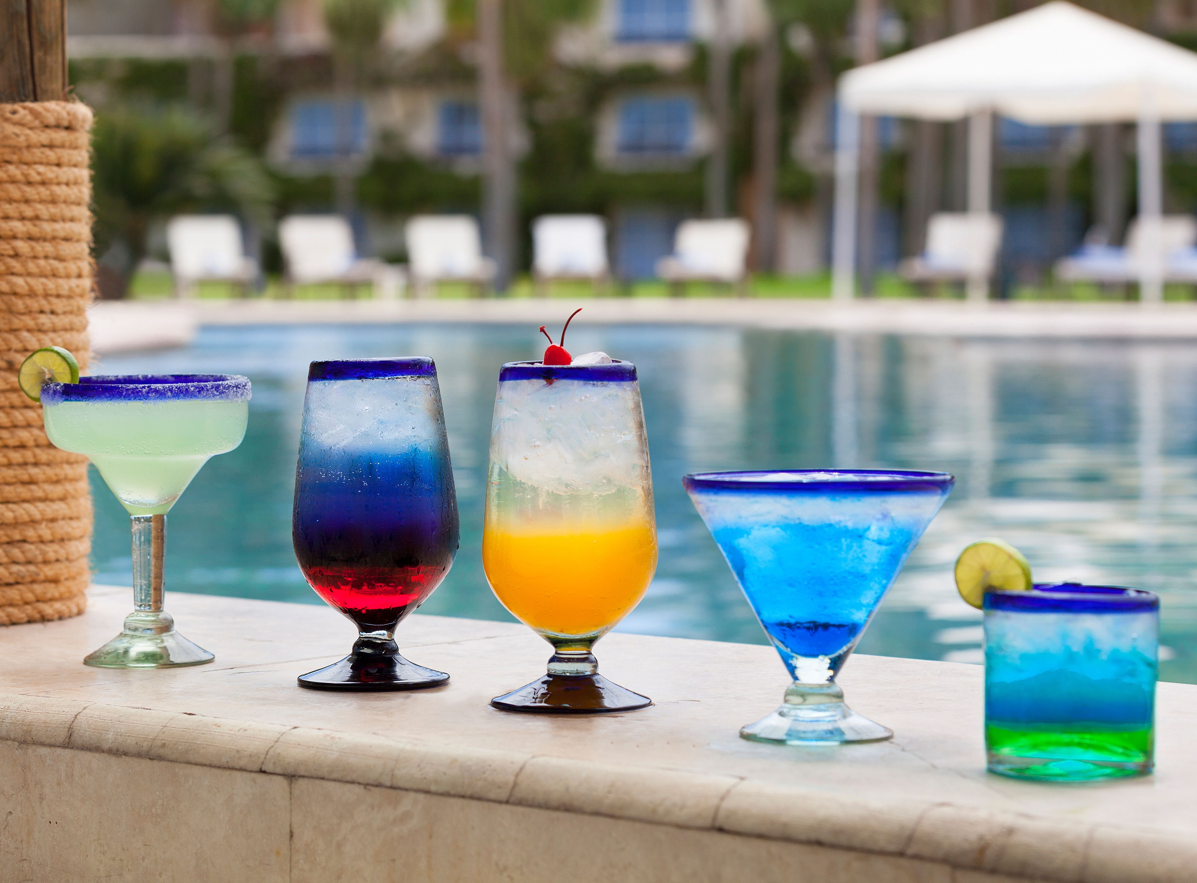 A row of colorful cocktails by a poolside.
