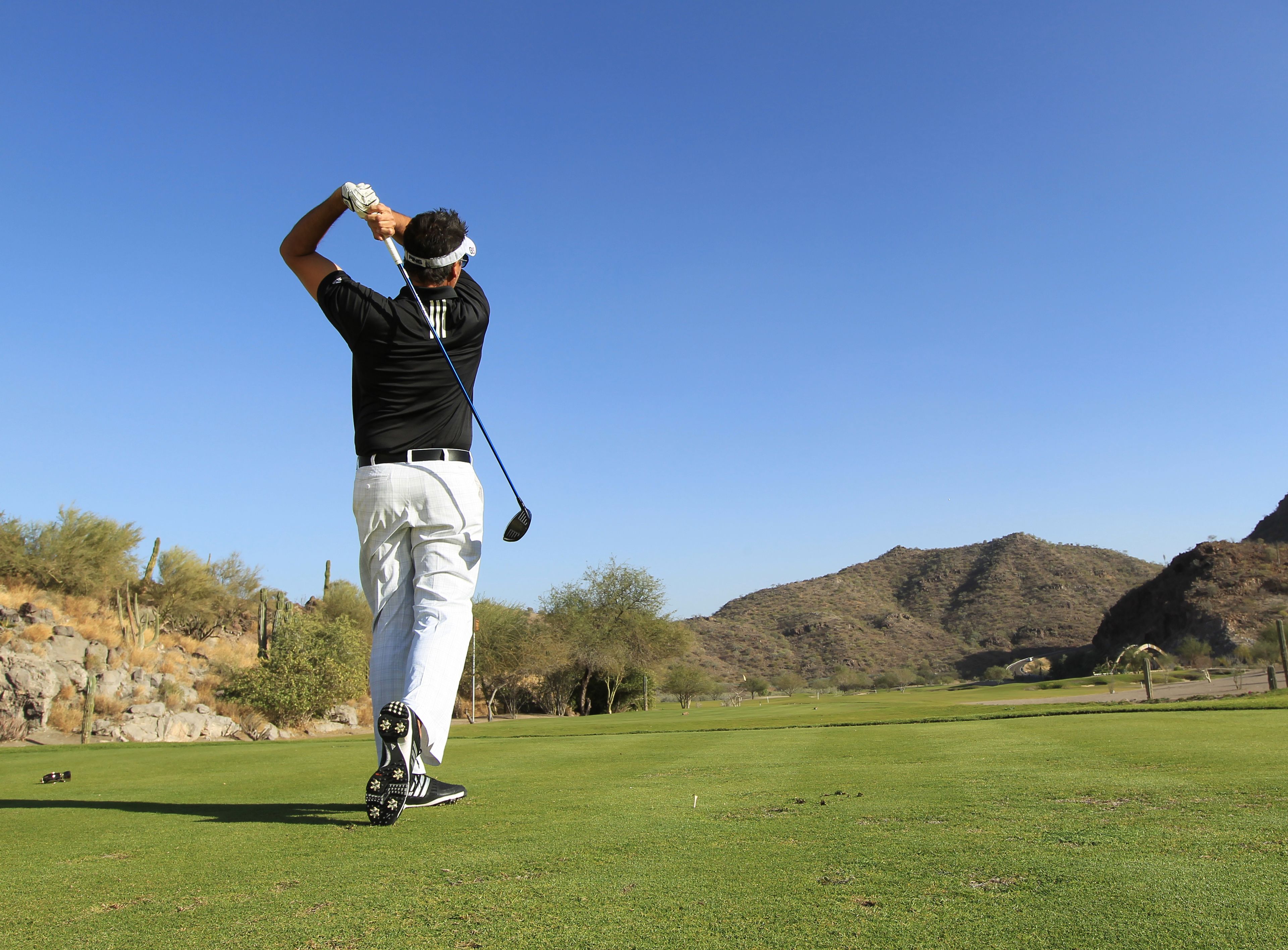 A person on a golf course with a clear sky and hills in the background.