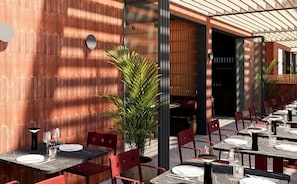 An outdoor dining area with tables and chairs, a potted plant, and a wooden wall.