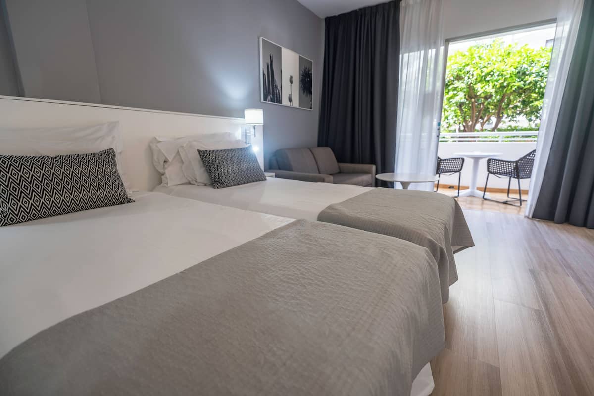A hotel room with two beds, a sofa, a small table, and a balcony with chairs.