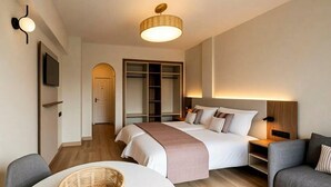 A modern hotel room with a bed, bedside tables, a TV, a wardrobe, and a seating area with a table and chairs. - Coral California (Arona)